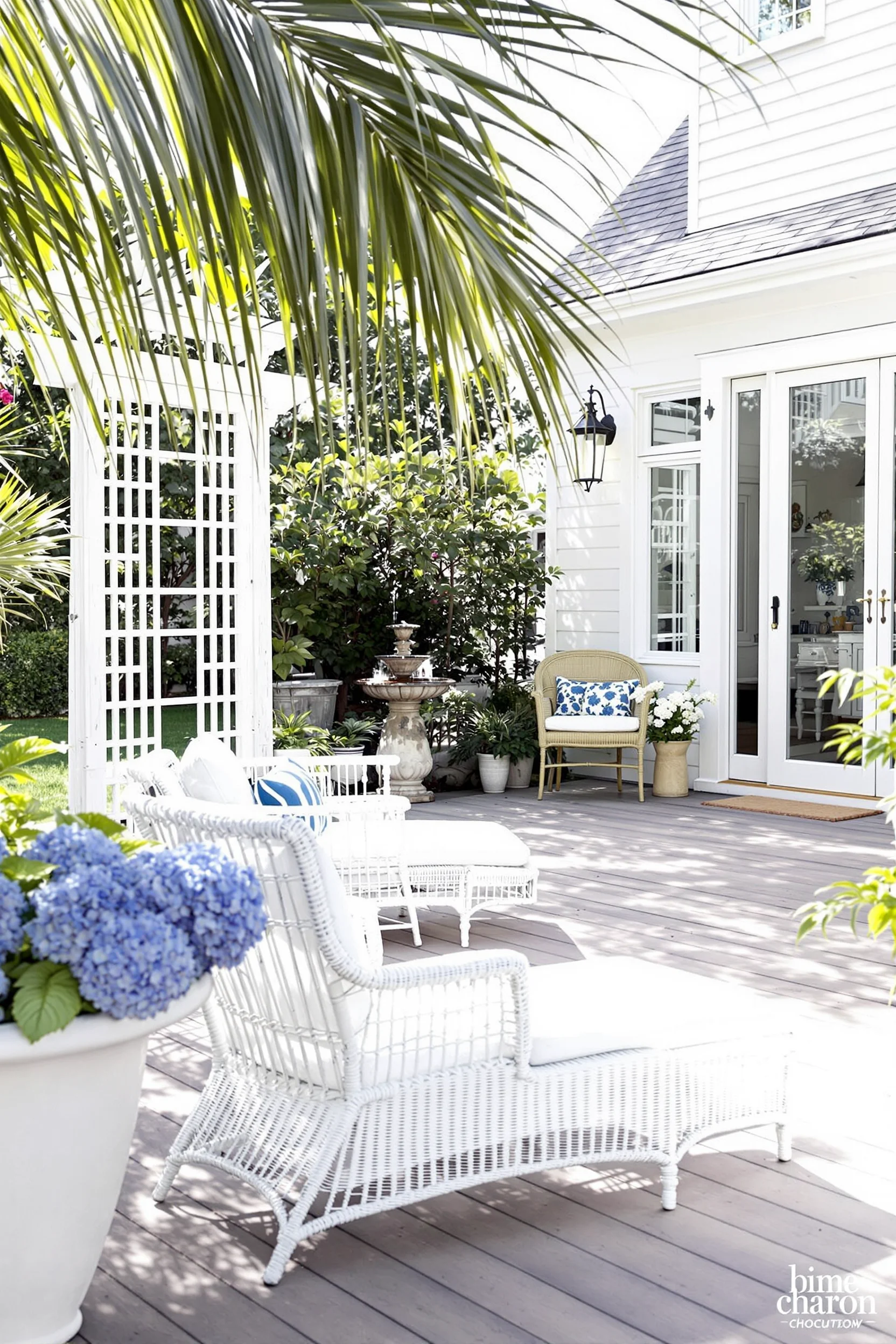 elegant hamptons coastal garden with white wicker chair blue hydrangeas stone fountain and french doors to interior
