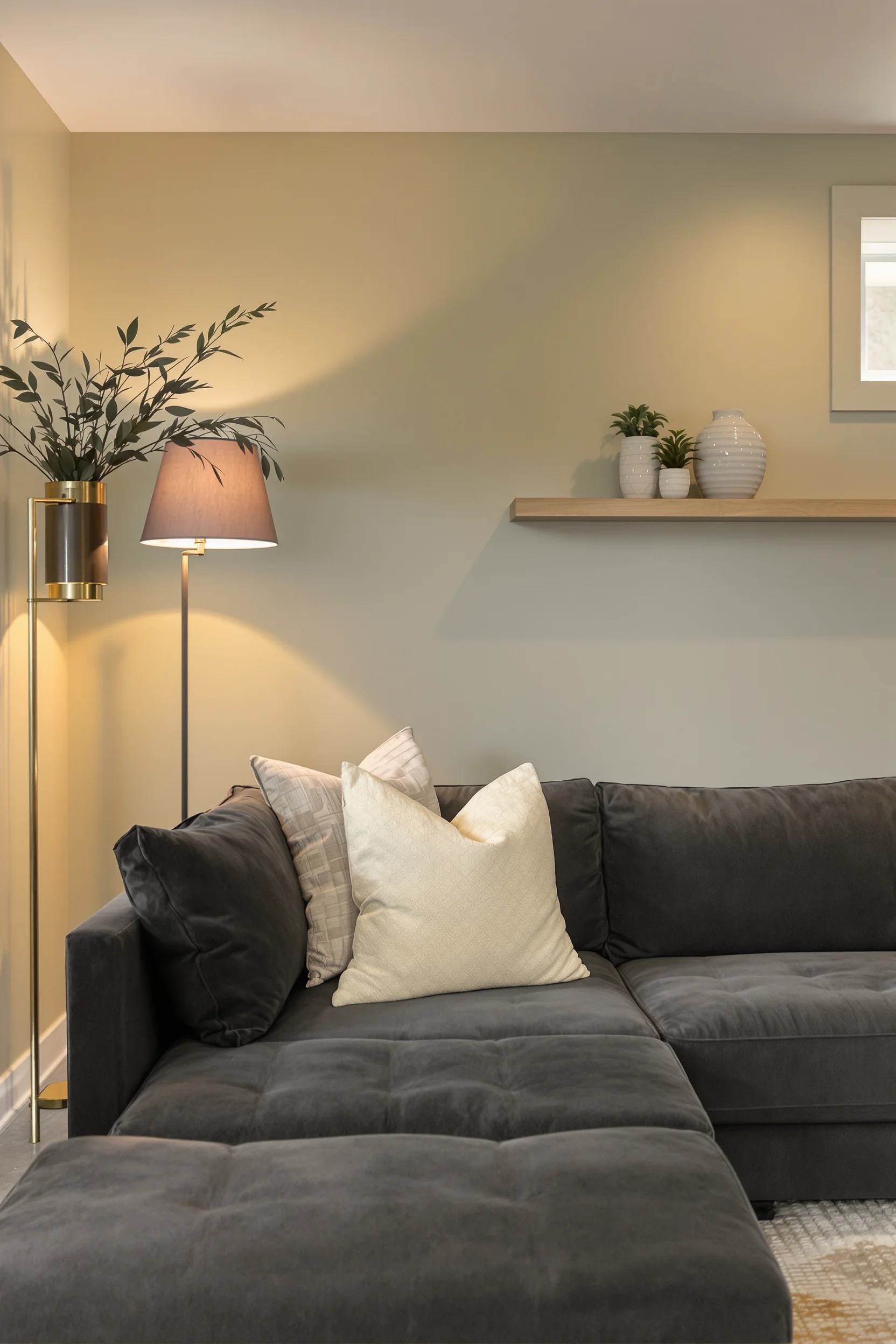 sage green cozy basement ideas featuring soft accent wall with dark charcoal sectional and warm lighting