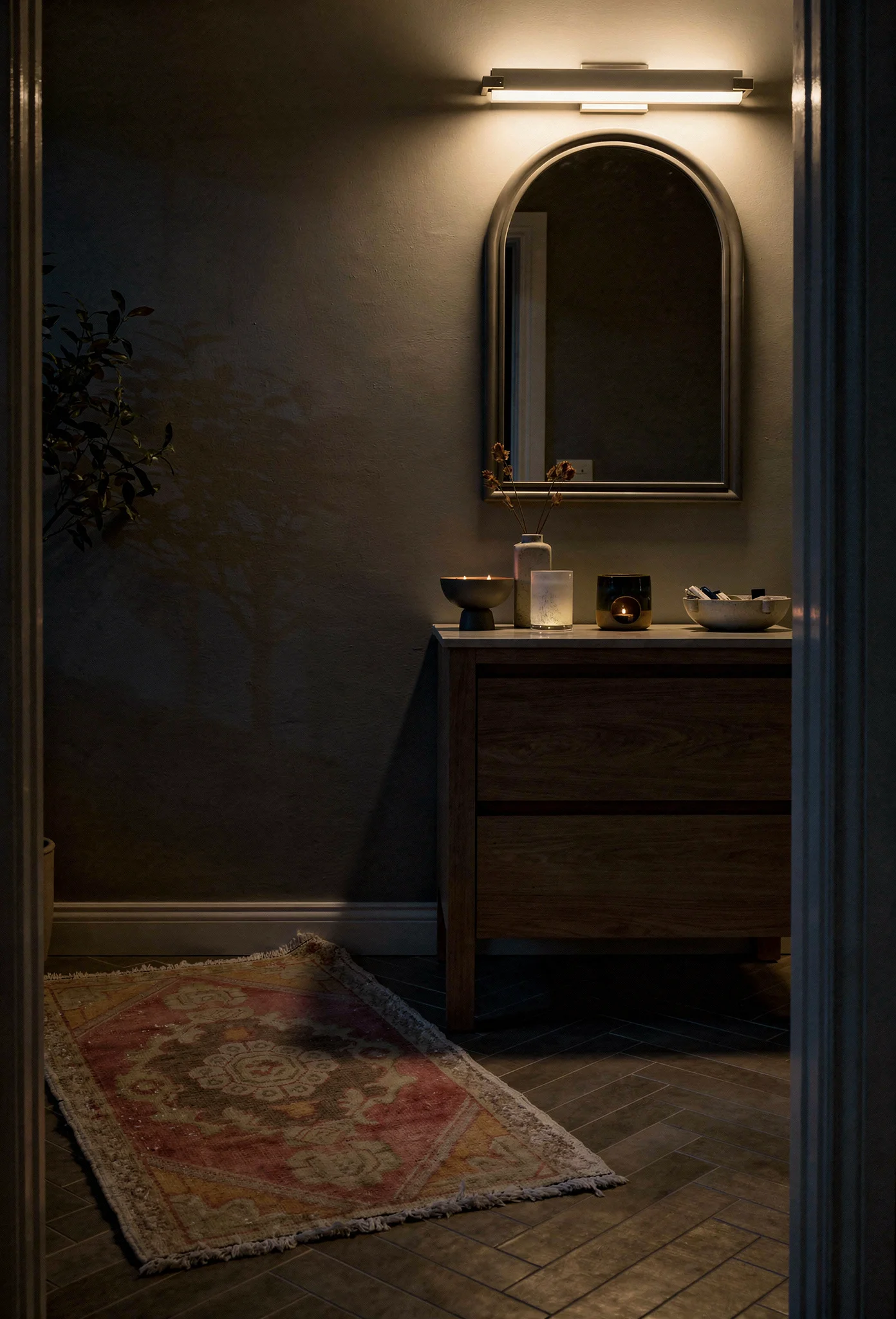 Modern small bathroom tile featuring grey arched mirror with herringbone wall and vintage Turkish rug evening mood