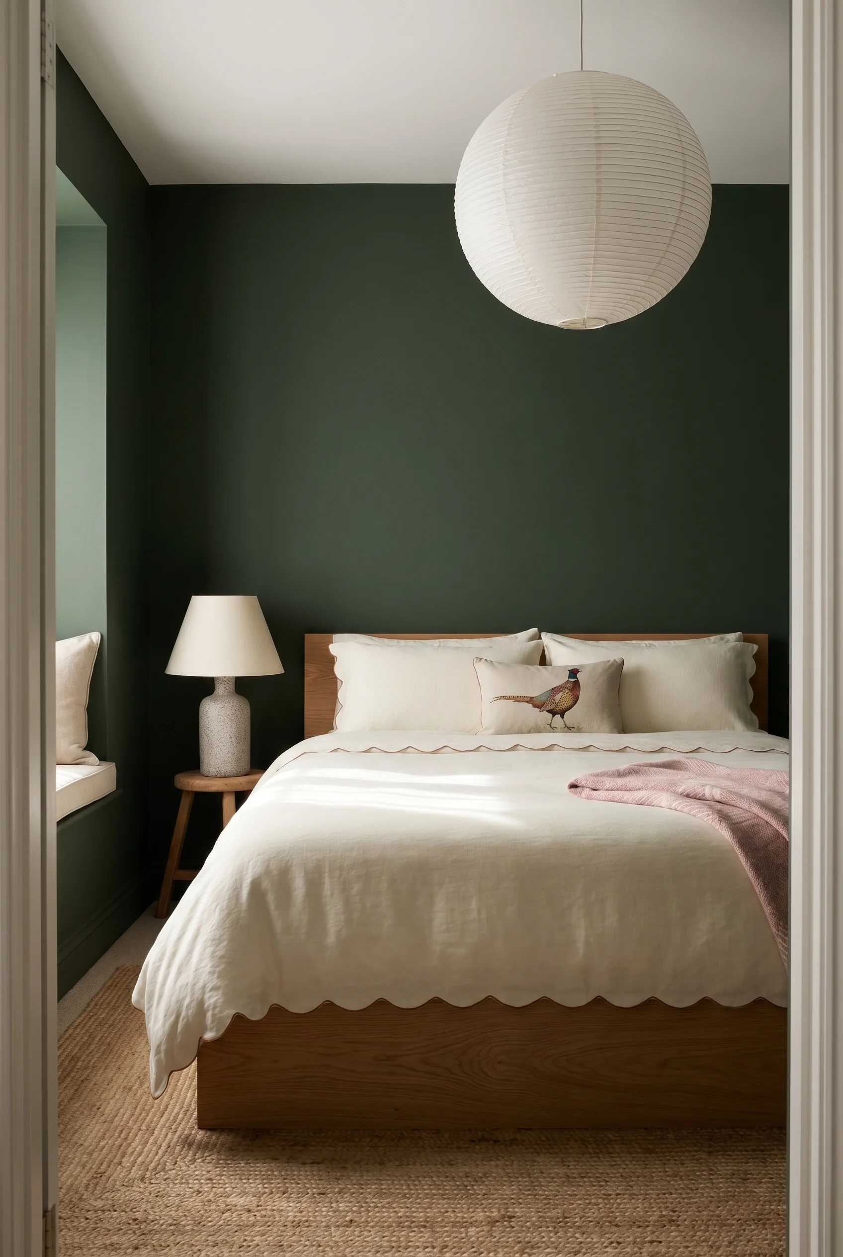 English Country Bedroom featuring oak platform bed with paper lantern pendant and folk pheasant cushion on deep forest green walls