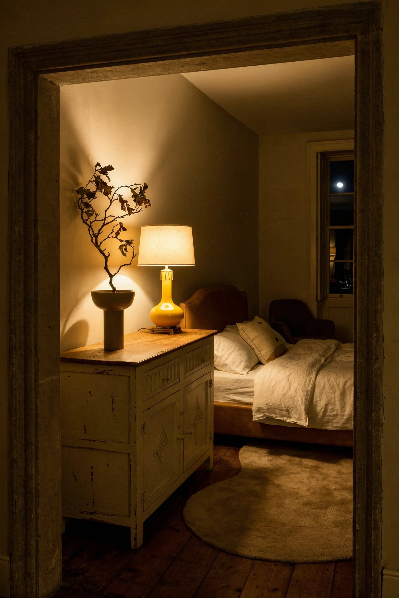 French Country Bedrooms featuring distressed cream dresser with yellow ceramic lamp through stone doorway evening mood