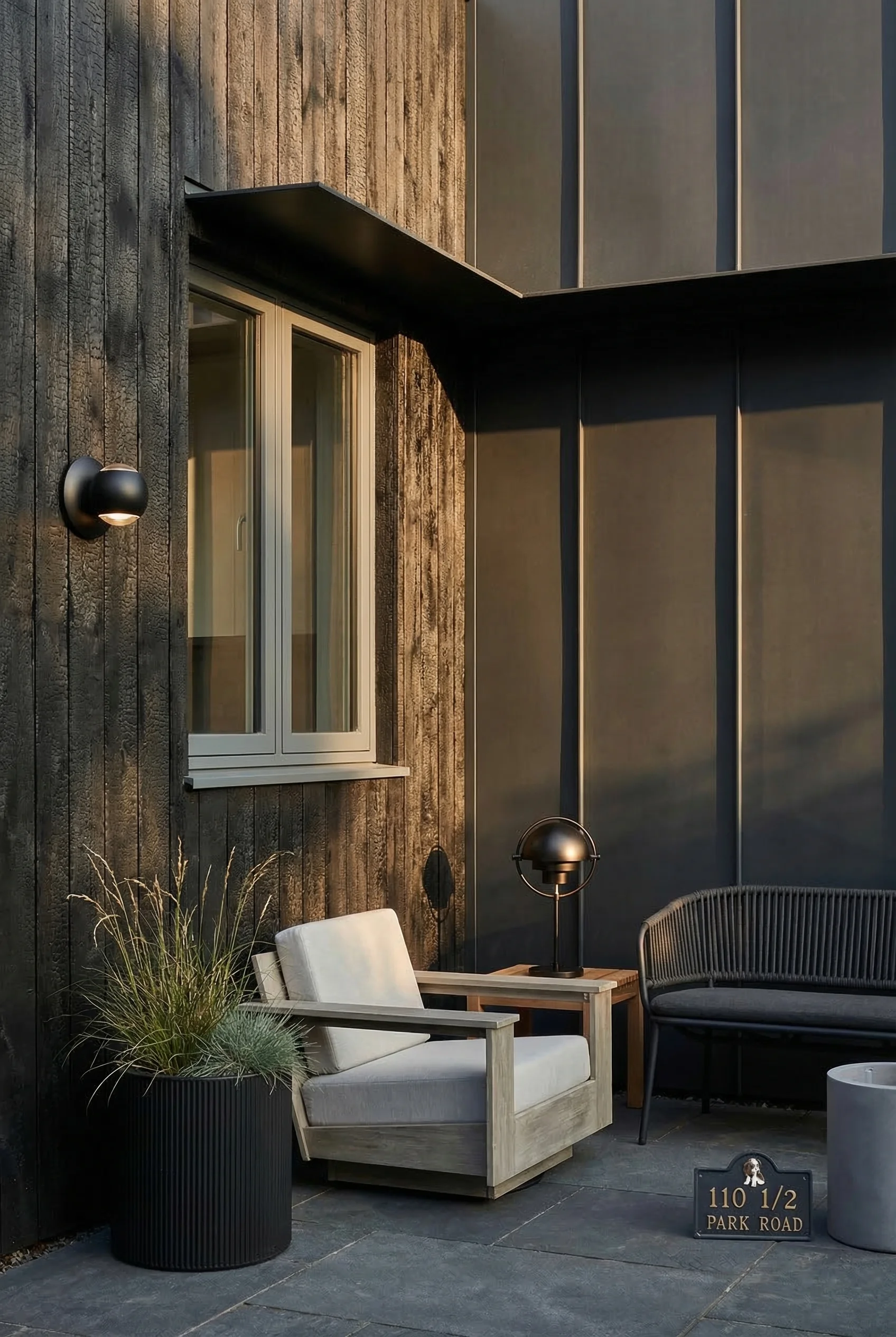 Modern exterior cladding featuring black hemisphere wall sconce with black cylinder planter