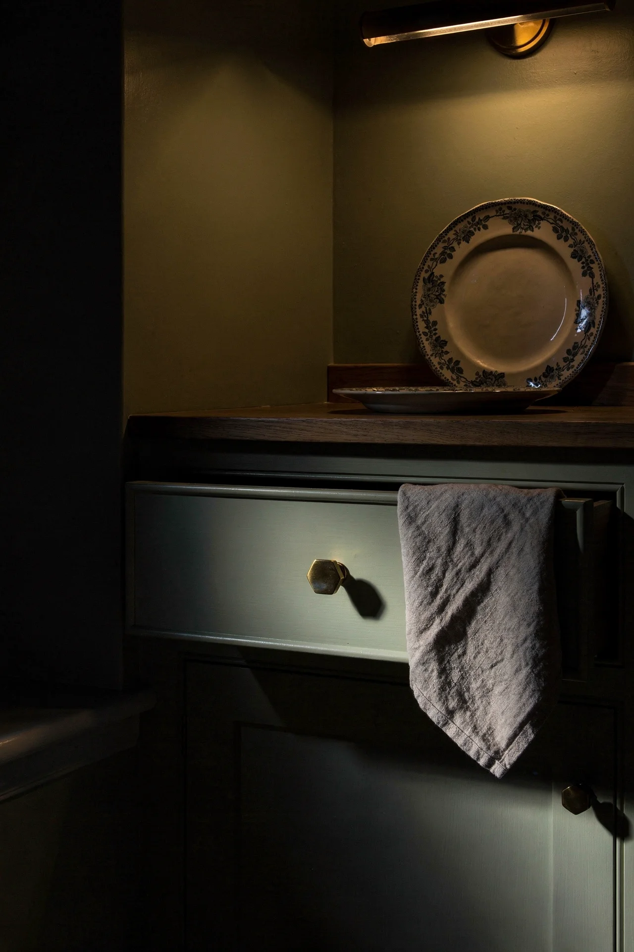 English country kitchen drawer detail with pale fern green cabinets and brass hexagon knob evening mood