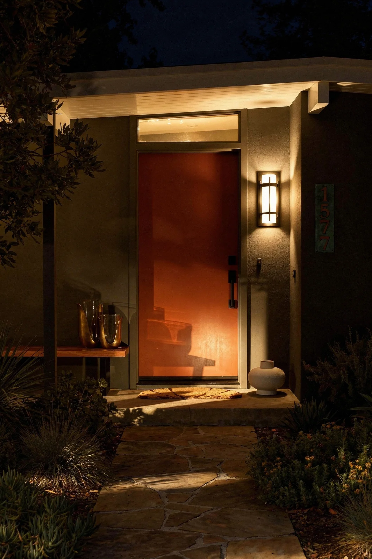 Mid century modern house exterior featuring burnt orange front door with copper address plaque on grey facade evening mood