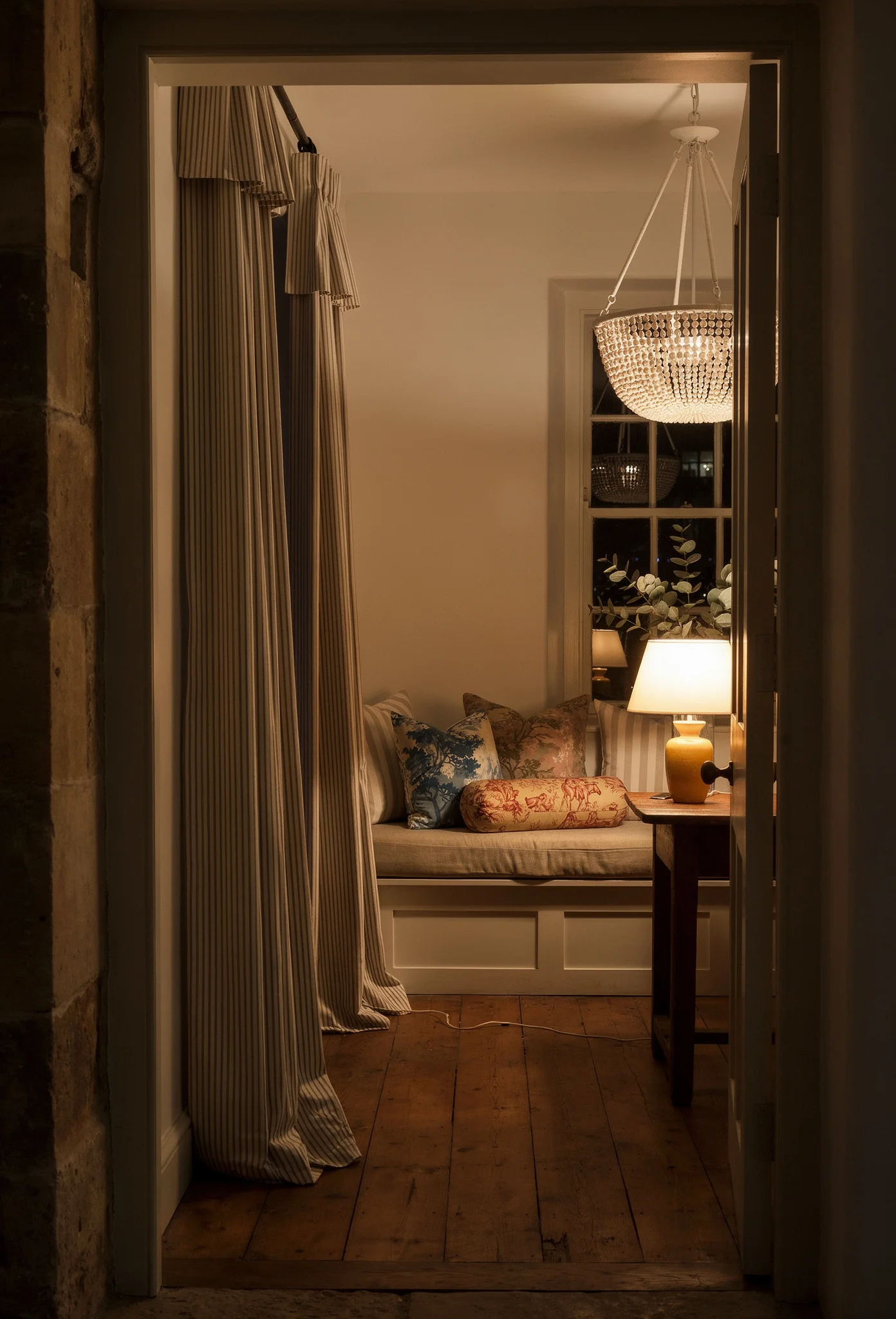 French country decor featuring ticking stripe curtains with toile pillows on cottage window seat evening mood
