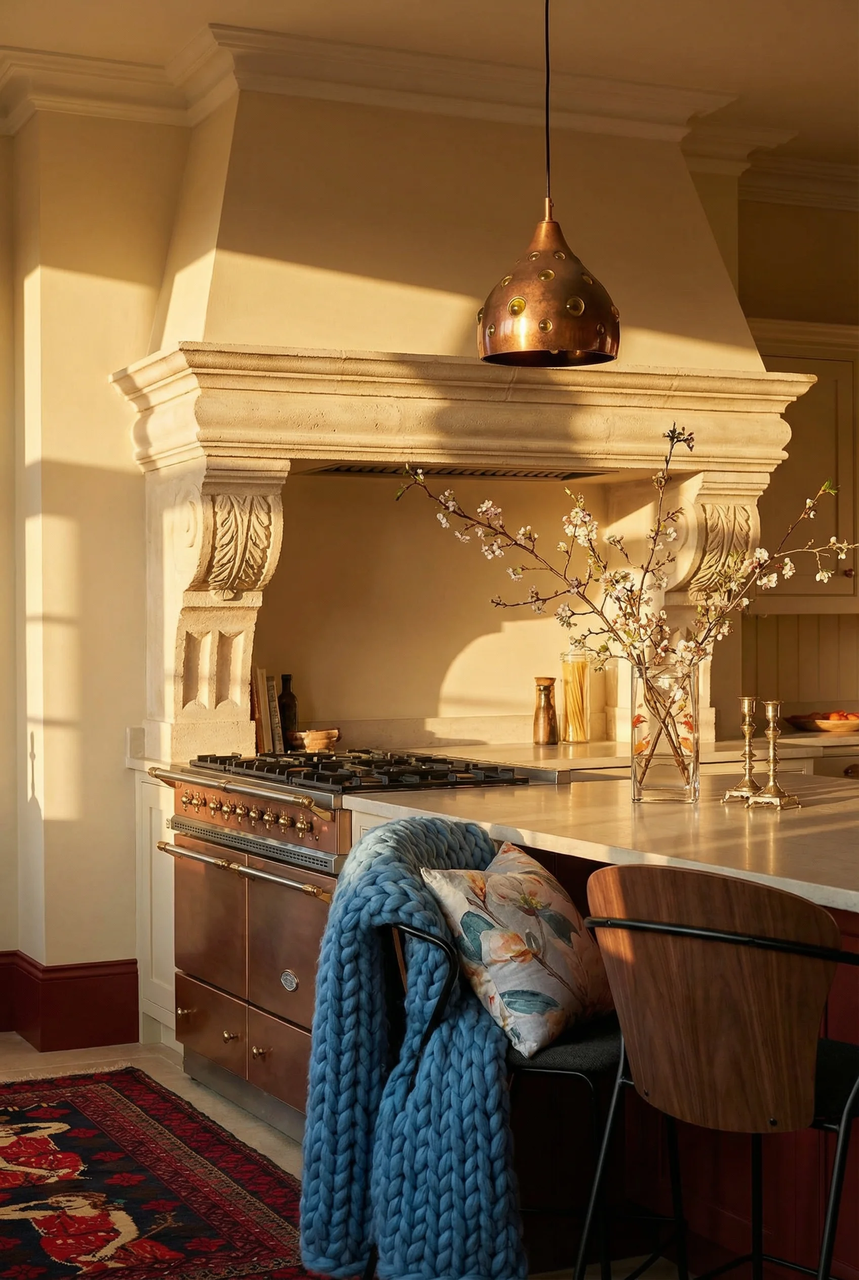 French Country Kitchens featuring carved stone range hood with vintage copper pendant and walnut dining chair