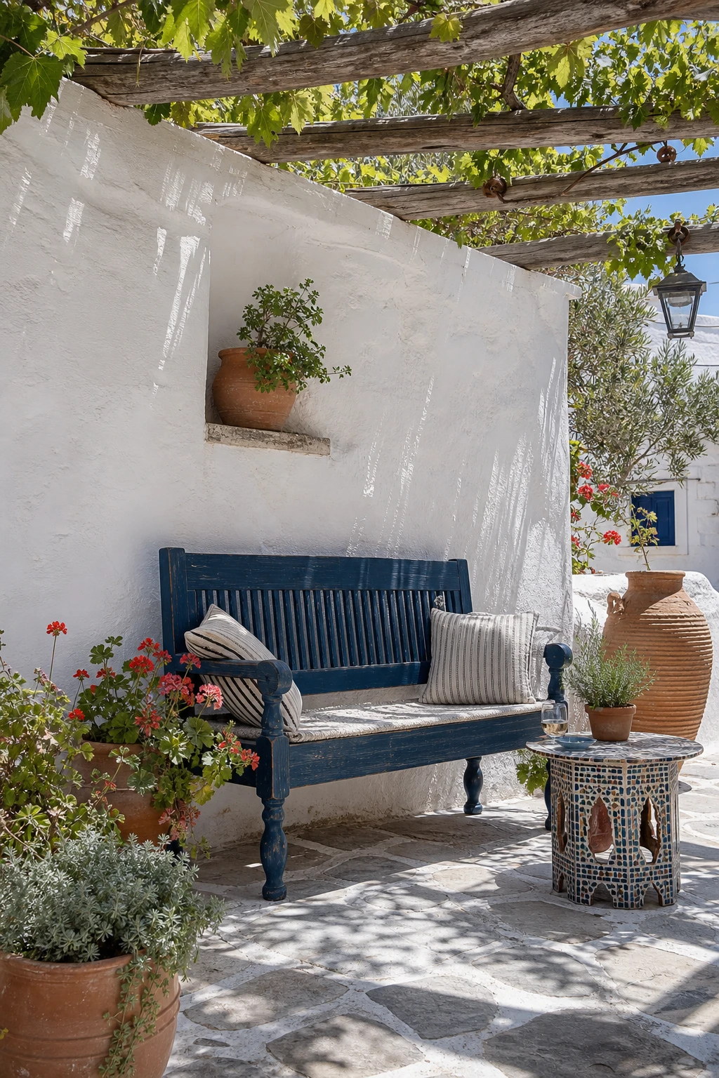 A Mediterranean Greek style garden with blue painted seating as the hero, terracotta pots, white rendered walls and dappled midday sunlight