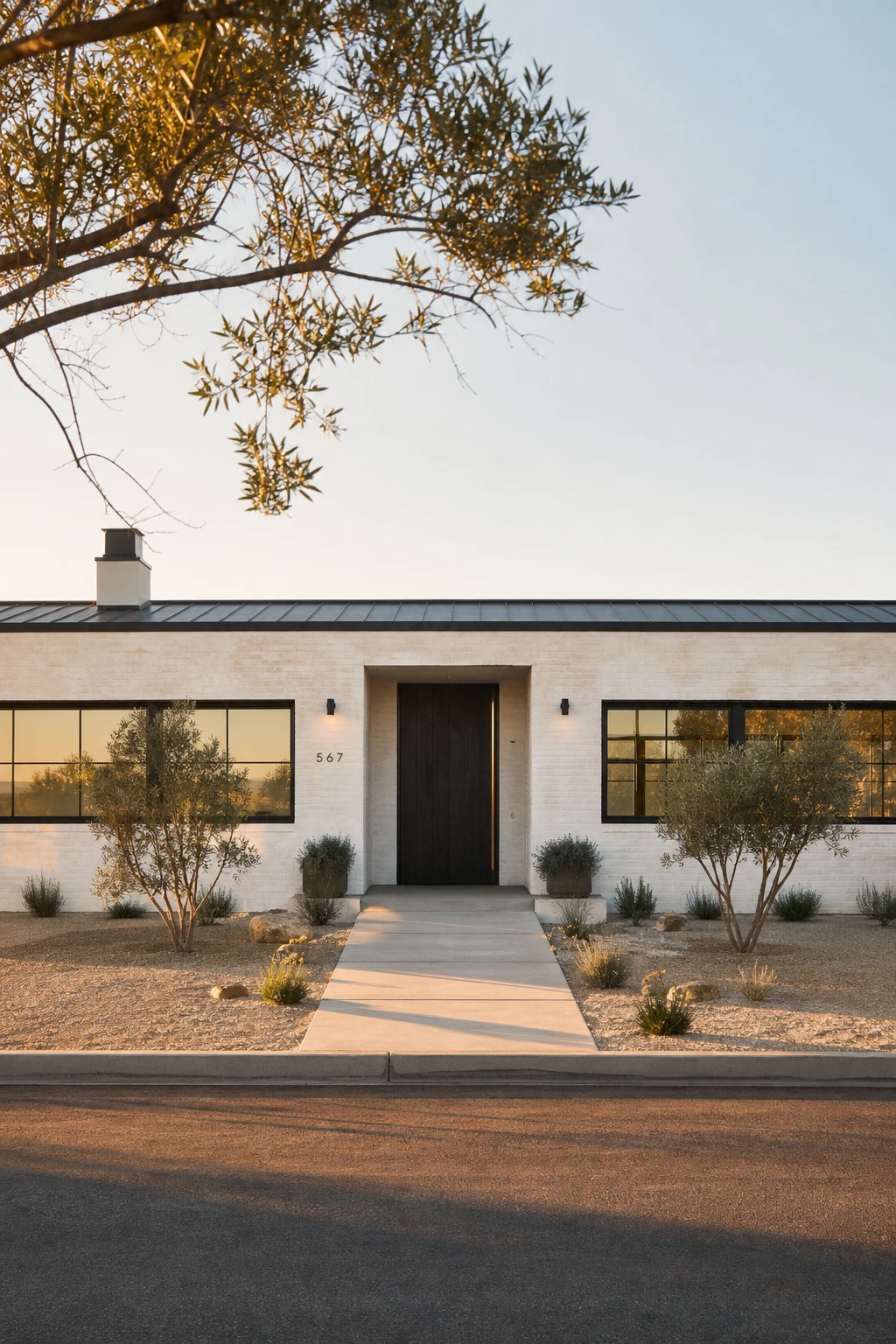 Black and white modern ranch exterior with limewash finish on brick facade, matte black trim, recessed entry and drought tolerant gravel landscaping in warm afternoon light
