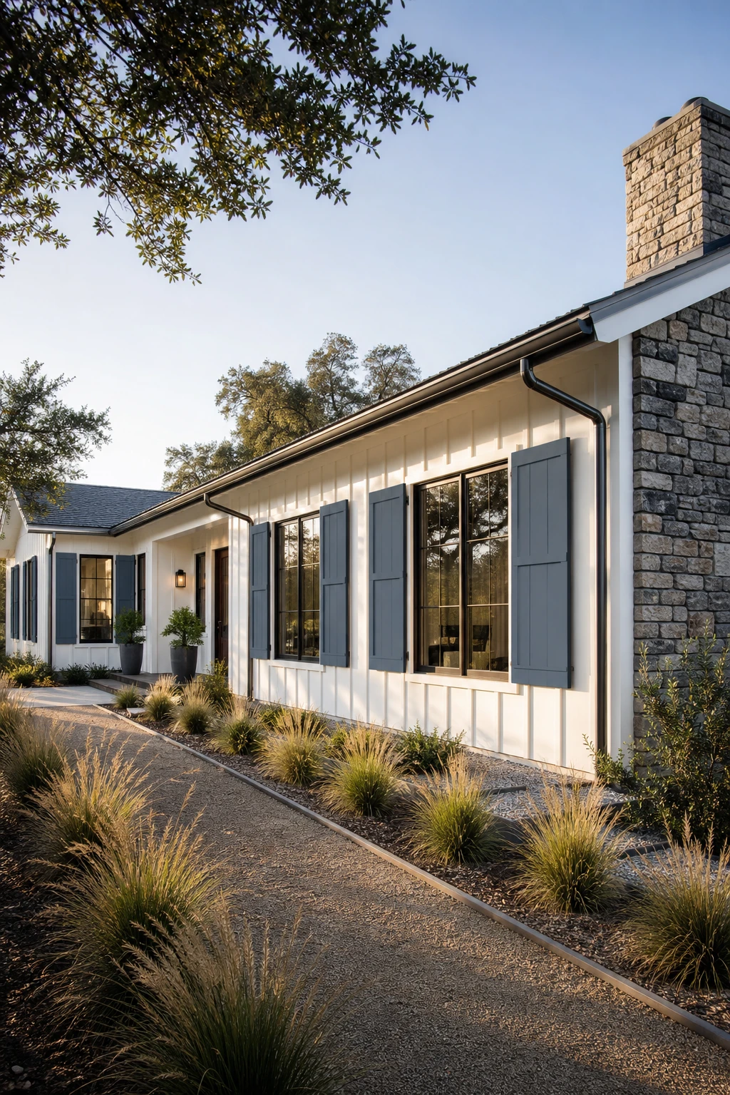 Blue Modern Ranch exterior with Oval Room Blue painted shutters framing wide windows, board and batten siding, a stone chimney, and a gravel path in afternoon light.