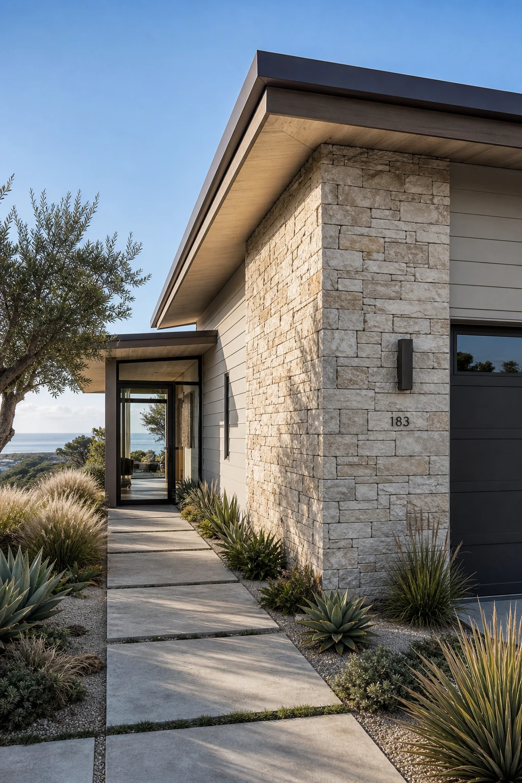 Coastal Modern Ranch exterior with a natural stone feature wall as the hero accent anchoring the low horizontal facade under soft midday coastal light