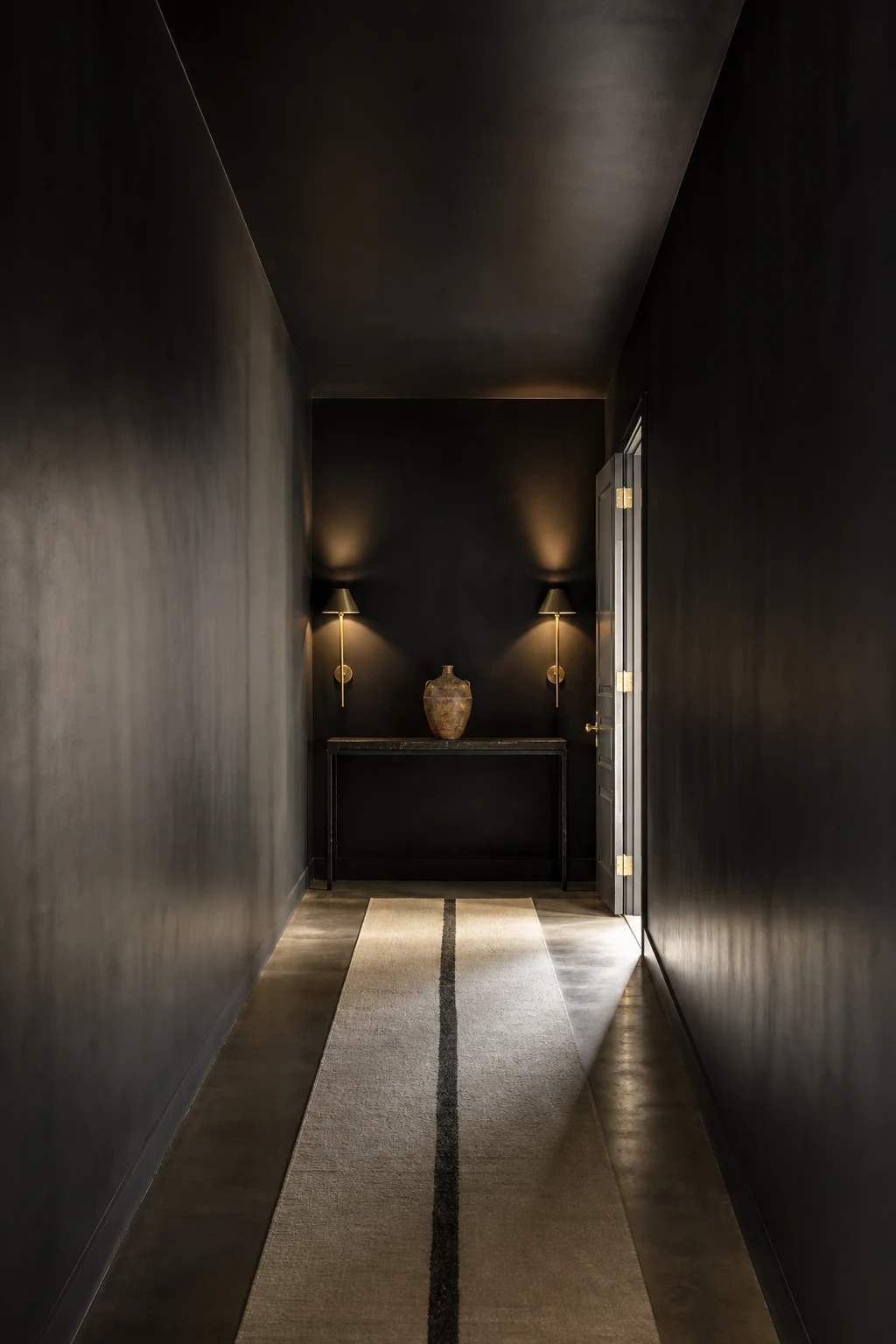 All black hallway with ceiling and walls painted the same deep black creating a cocoon effect with soft sconce lighting and a pale runner