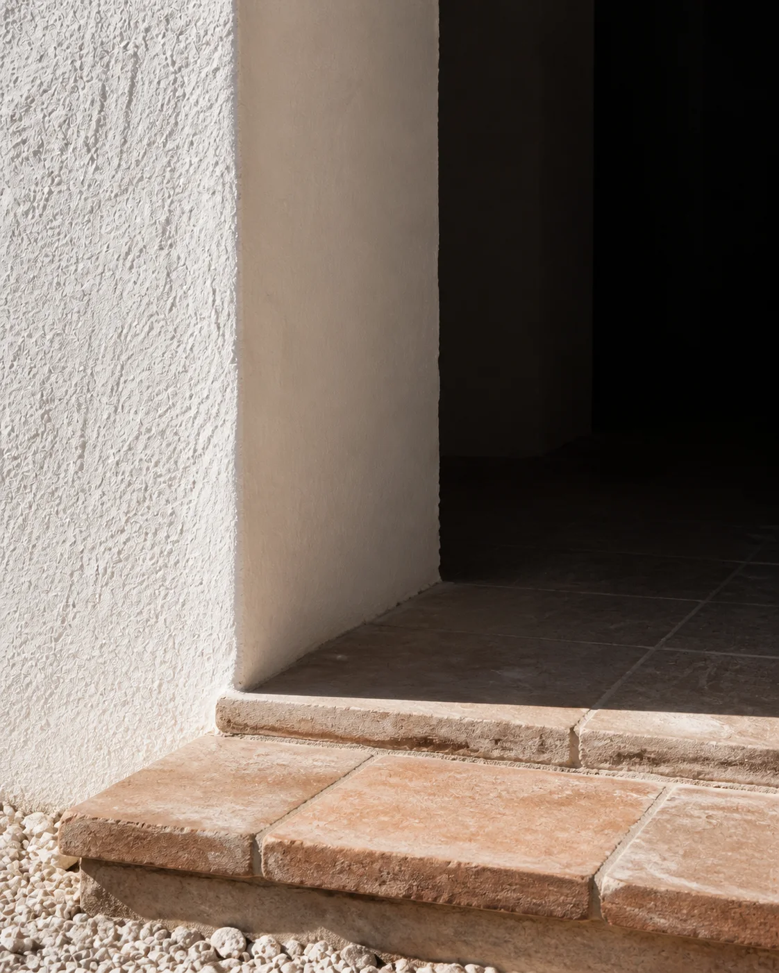Close detail of a deep white plaster arch terracotta step shadowed passage pale aggregate and hard southern sunlight in the Milos house part of an editorial architecture view study