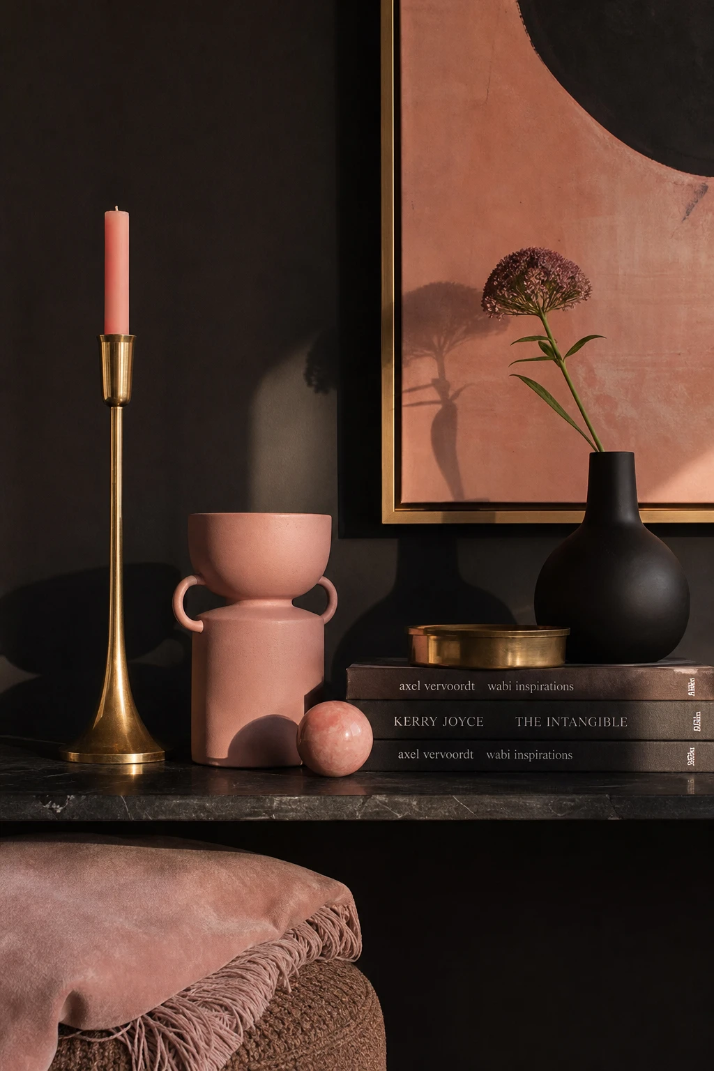 Close up vignette of a black and pink styled shelf with elegant decor details including sculptural objects, brass accents, and velvet textures in soft pink and black tones