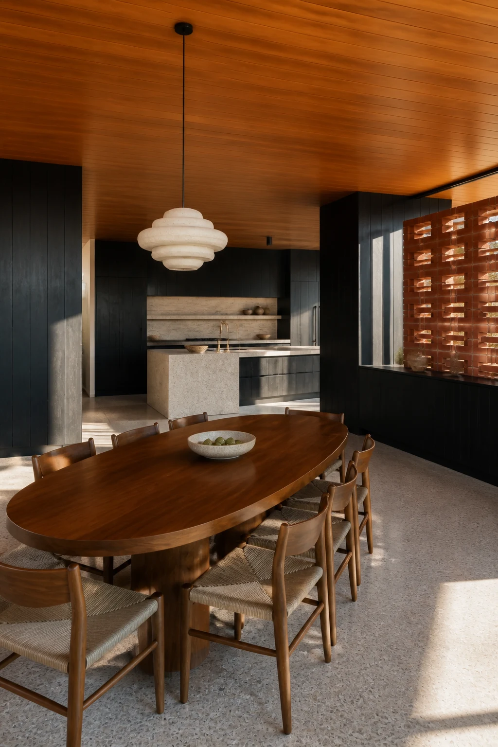 The walnut dining table and woven chairs looking back to the same black timber kitchen and pale island.