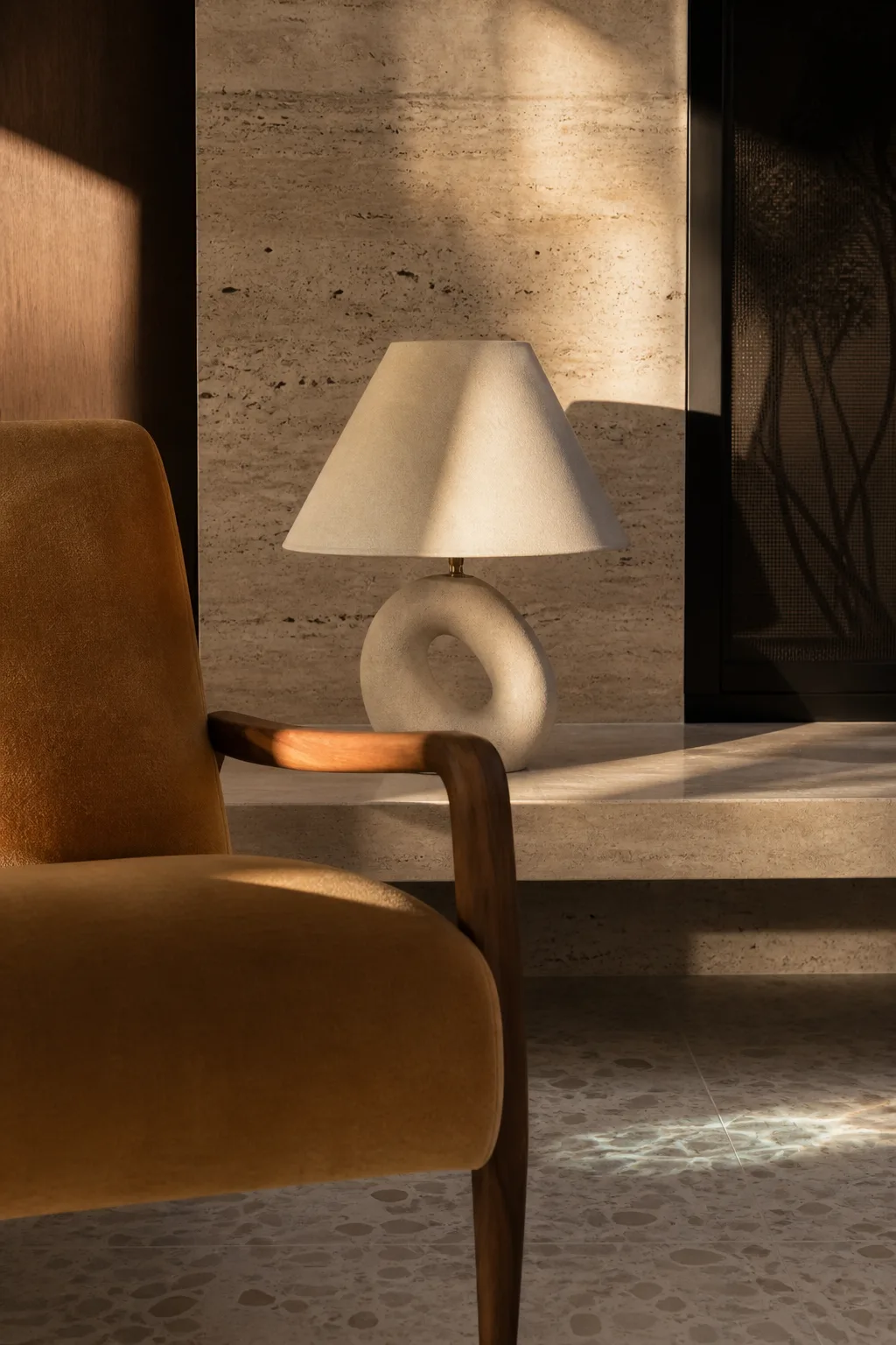 A camel chair, walnut arm, travertine hearth and ceramic lamp in the Palm Springs living room.