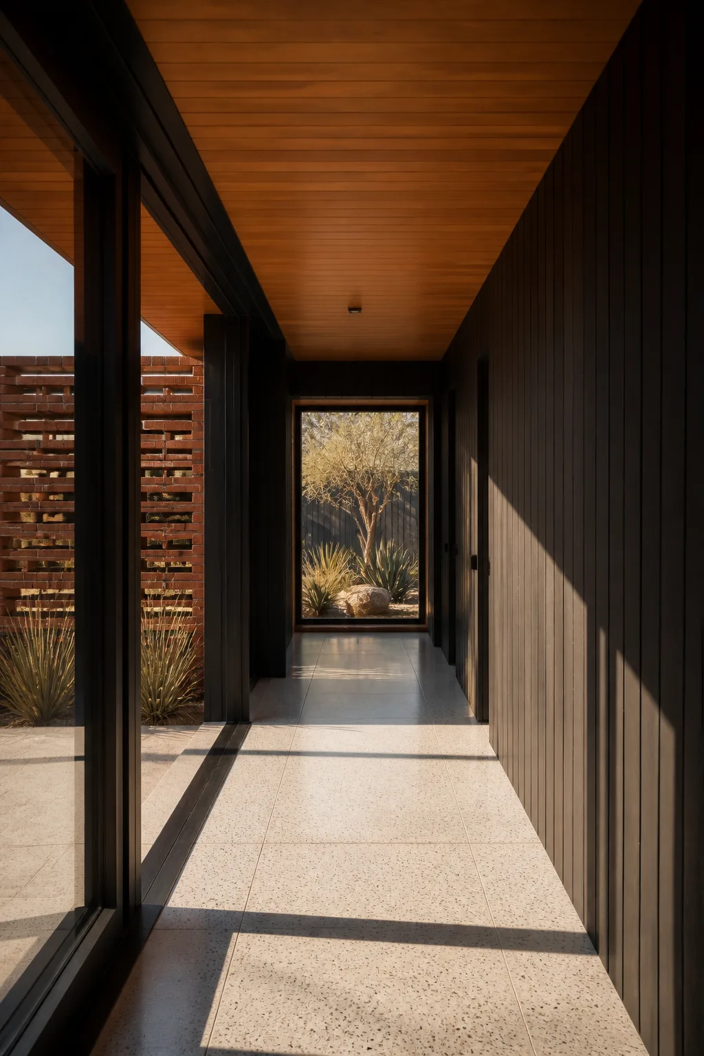 A long hallway with black timber walls, warm timber ceiling, terrazzo floor and a framed olive tree view.