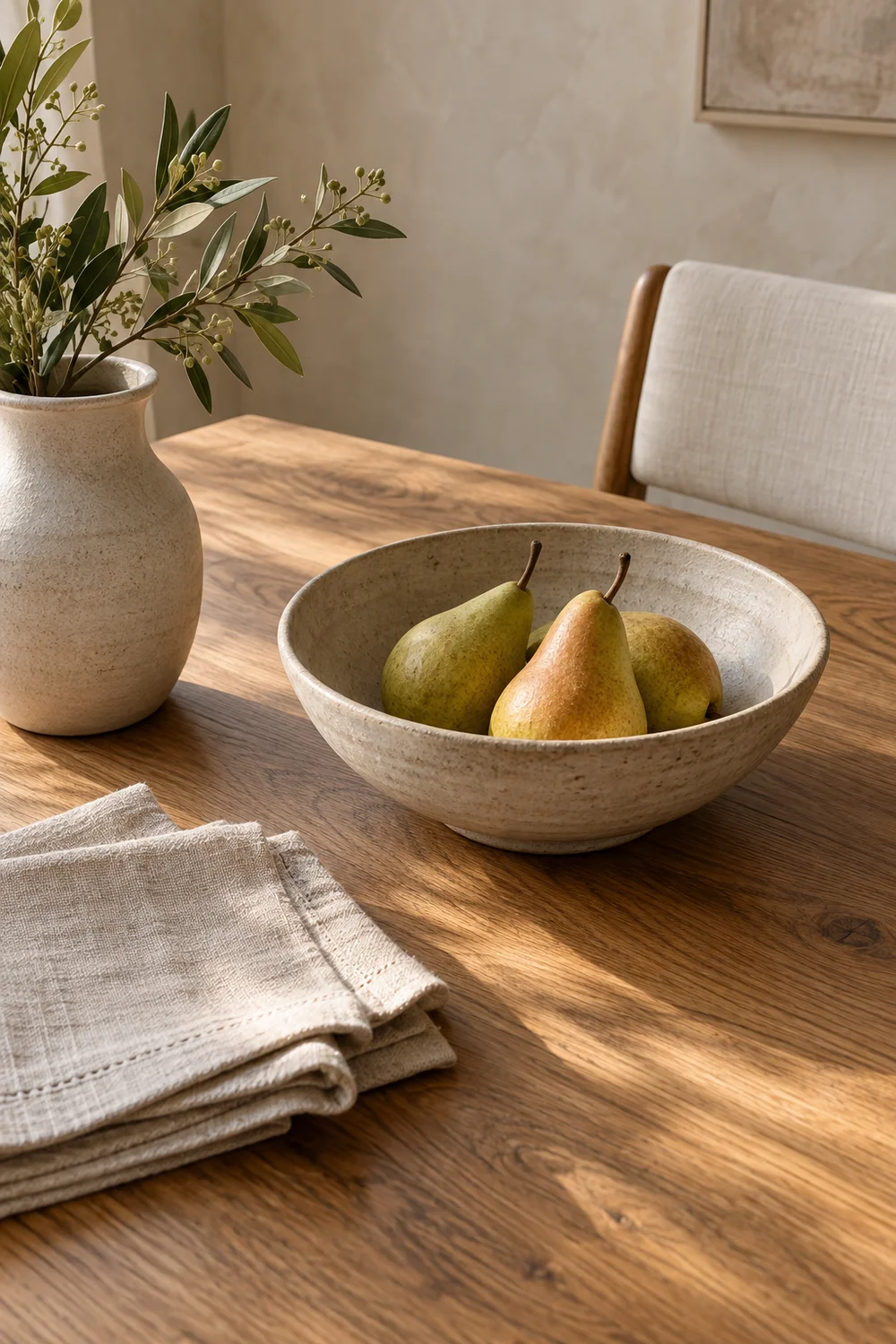 Pears linen napkins and ceramic vessel on oak table.
