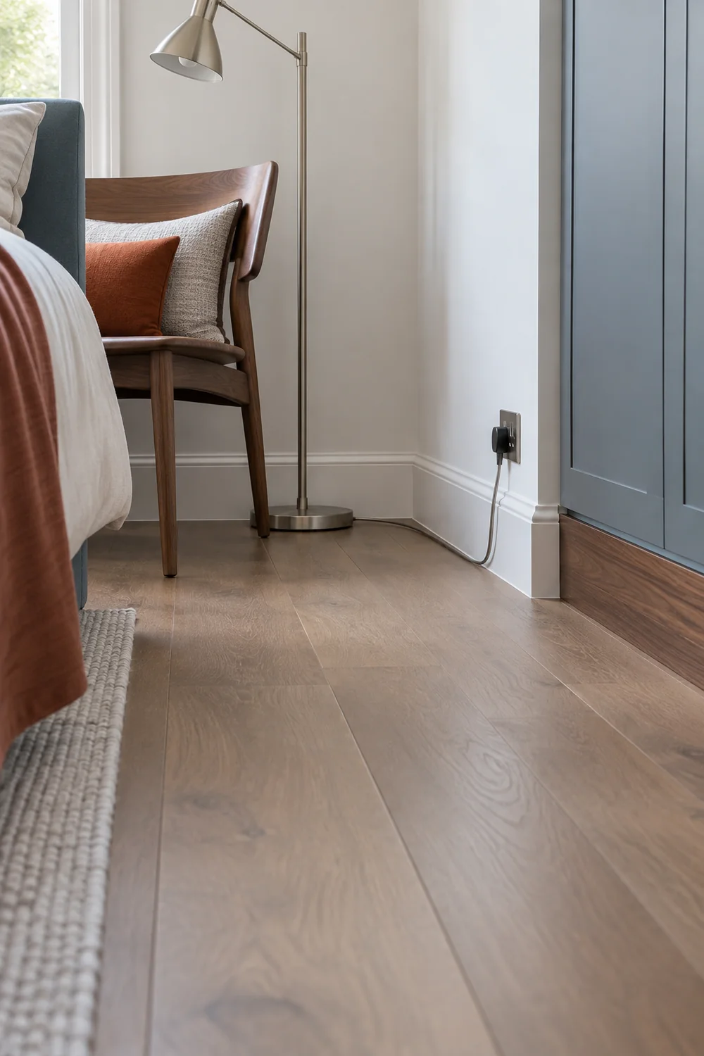 Reading lamp cord following the baseboard behind a small bedroom chair