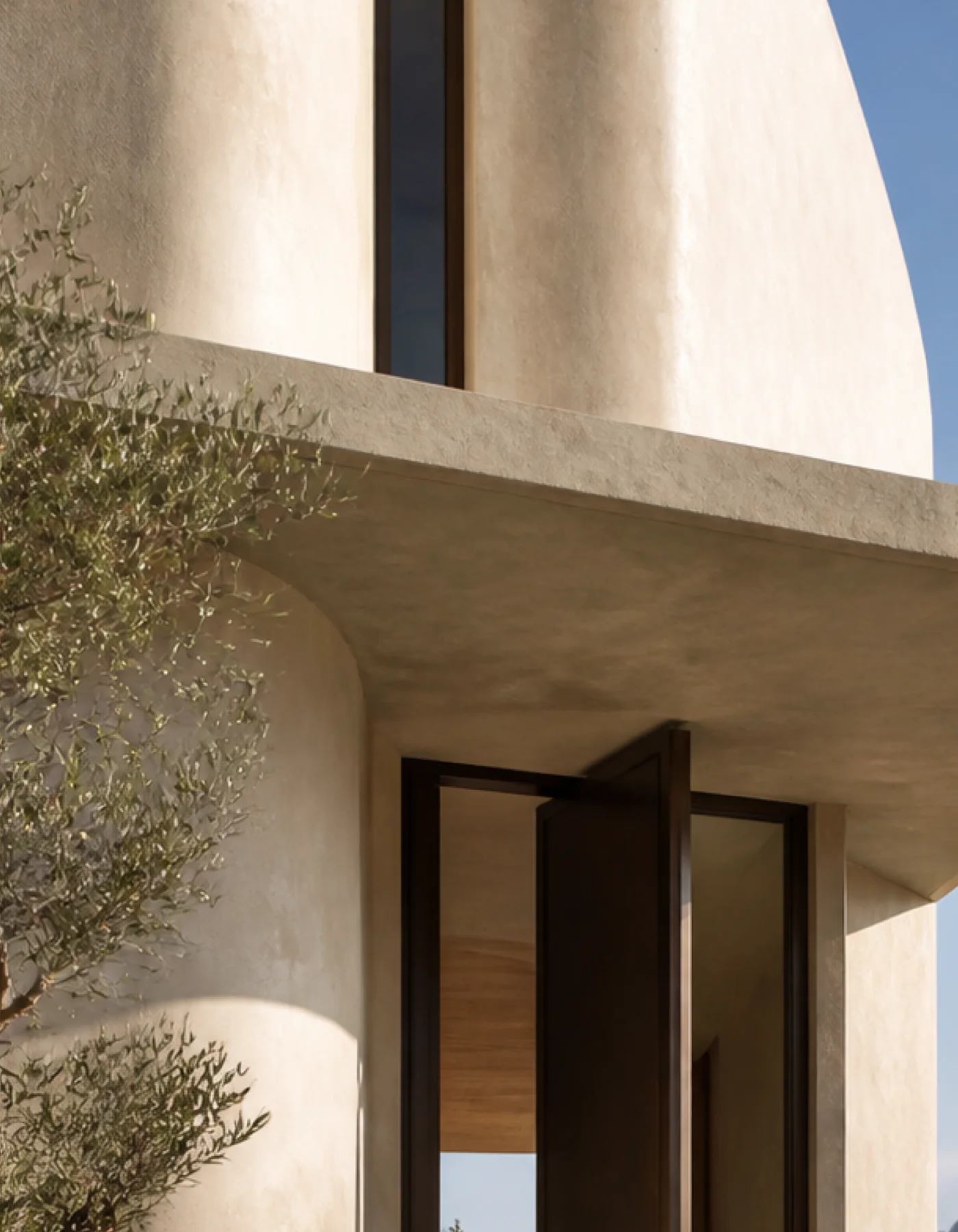 Pale limestone and the shaded curved canopy of the Cala d’Hort house beside its bronze entrance and olive planting. This original fictional Cala d’Hort architecture study records..