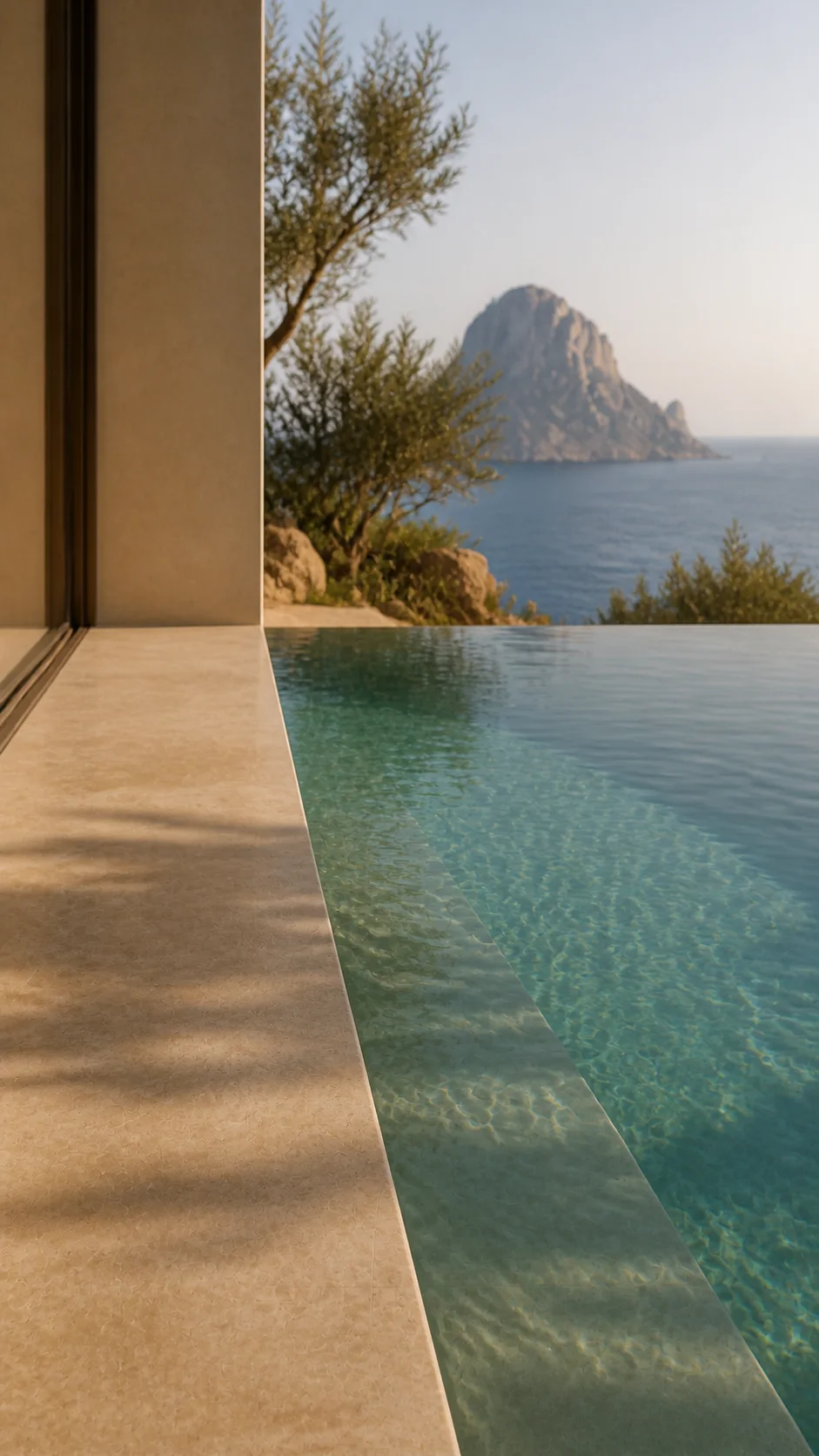Pale limestone infinity pool edge and clear water at Cala d’Hort with olive branches and Es Vedrà beyond. This original fictional Cala d’Hort architecture study records material,..