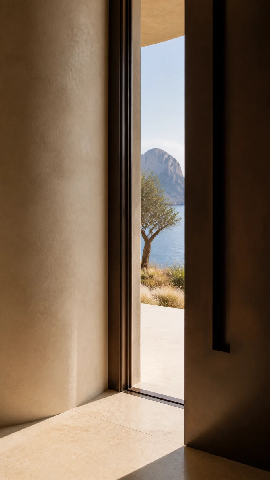 Bronze threshold and pale limestone floor of the Cala d’Hort house framing an olive tree, sea and Es Vedrà beyond. This original fictional Cala d’Hort architecture study records...
