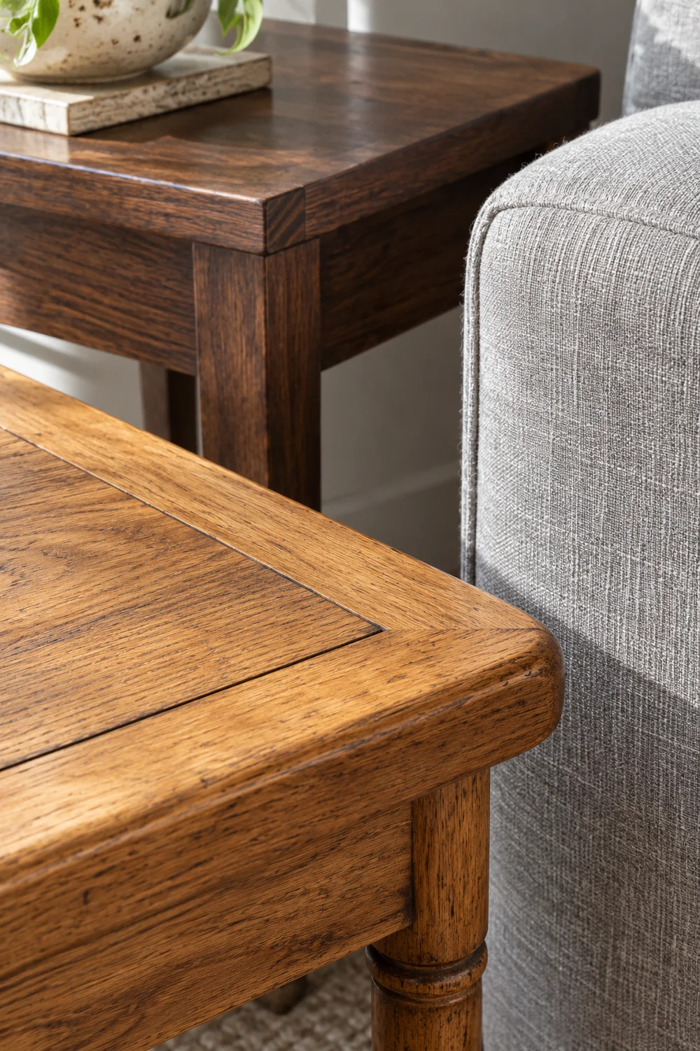 Honey oak and dark walnut table corners beside grey linen upholstery